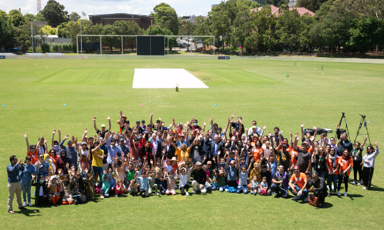 A large group of people with hands up standing on a field 