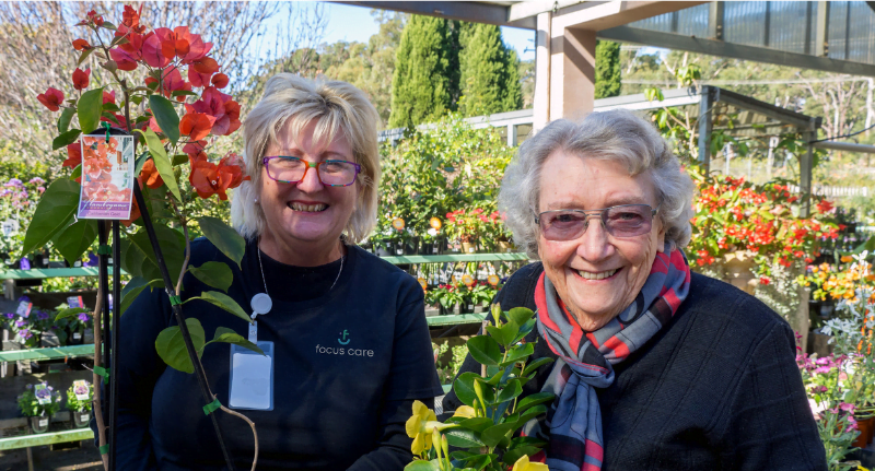 Two ladies smile amidst many flowers