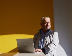 older genlteman sitting at a laptop looking out towards the sun