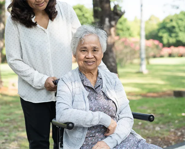 Elderly woman in a wheelchair with carer at the park.