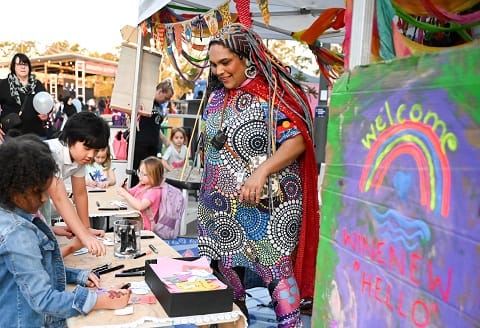 Woman in cultural dress at her market stall with kids doing art.