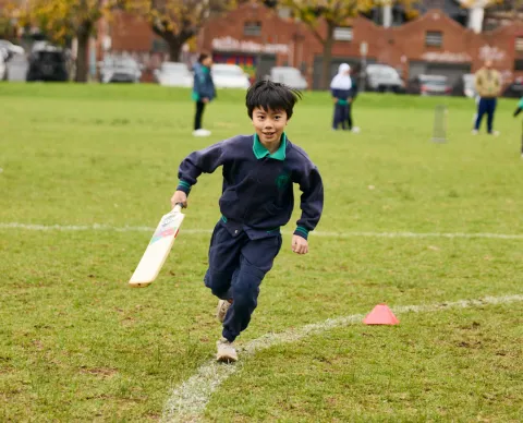 Melbourne school student running with bat during cricket activities for Refugee Week event
